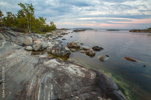 The gently sloping rock. White nights in Karelia. Rocky coast. The shore is strewn with stones. The natural landscape of Russia. Nature of Karelia. Ladoga lake.