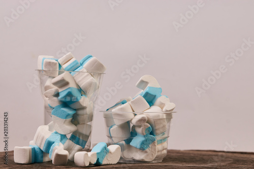 Marshmallow in a plastic glass on wooden table background, close-up. Sweet unhealthy snack