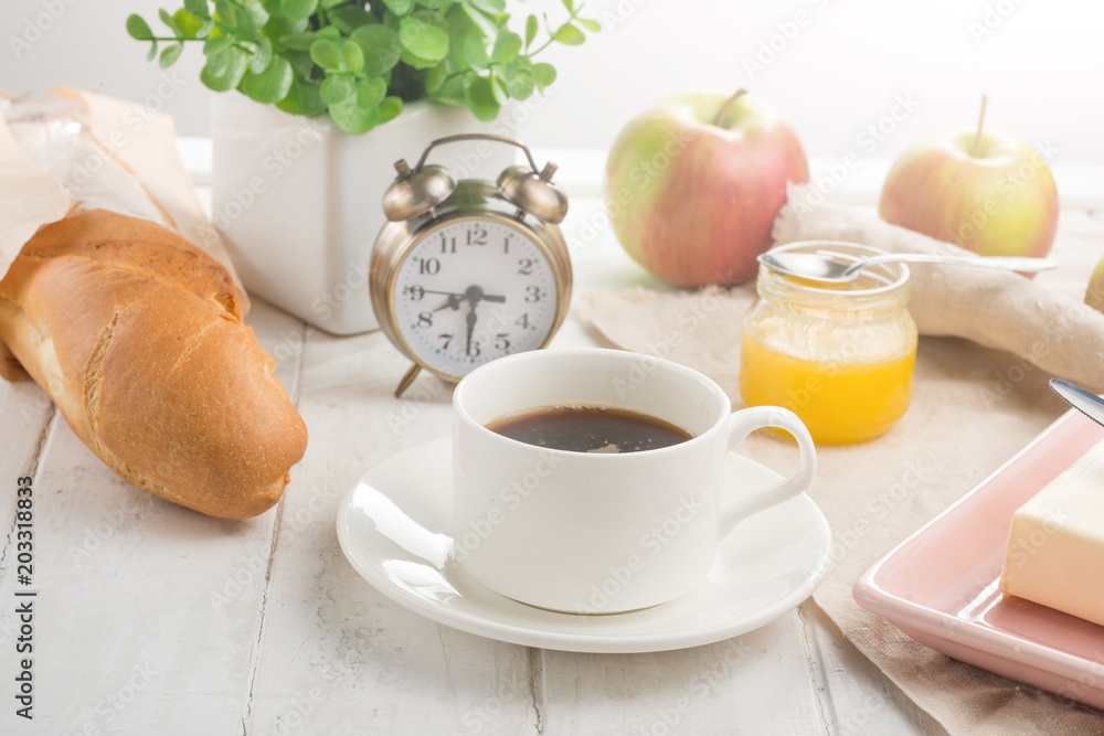 Morning cup of coffee, alarm clock, apples, butter and baguette, in a light kitchen. Background area, the concept of a bright morning and breakfast Morning cup of coffee, alarm clock, apples, butter and baguette, in a light kitchen. Background area, the concept of a bright morning and breakfast