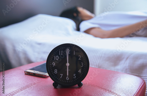 Close up of alarm clock with woman sleeping on bed in the bedroom blur background