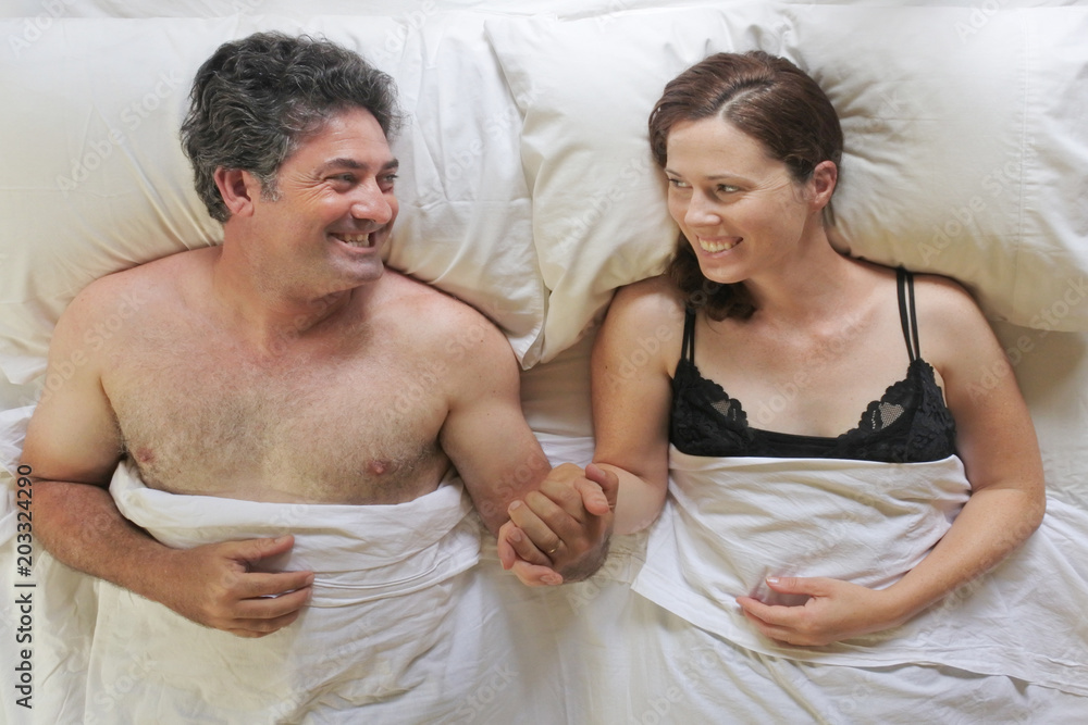 Above view of happy man and woman holding hands lay in bed Above view of happy man and woman holding hands lay in bed