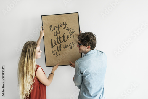 Caucasian couple hanging a frame on white wall