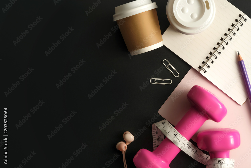 Styled stock photography of fitness equipment dumbbells notepad pencil and earphone on black background. Flat lay.