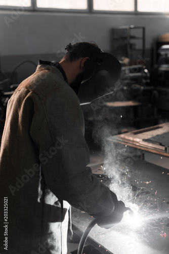 side view of manufacture worker welding metal with sparks at factory