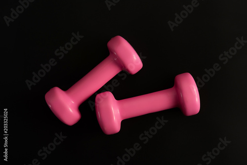 Two pink dumbbells isolated on black background. Top view. Flat lay