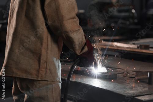 cropped shot of of manufacture worker welding metal with sparks at factory