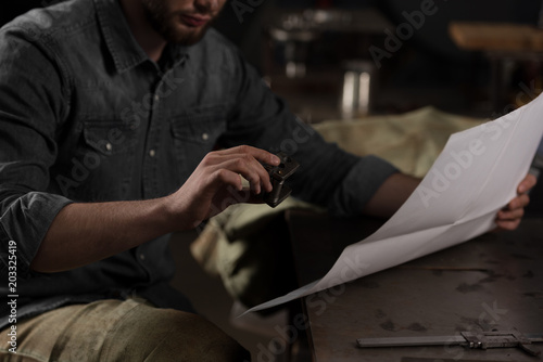 cropped image of young male worker sitting with blueprint at factory