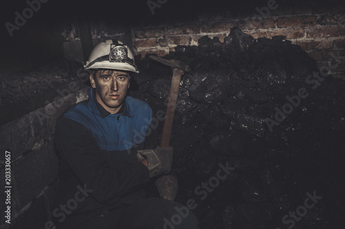 a miner with a pick sitting on the corner all tired and dirty from the coal dust after a hard work in the mine