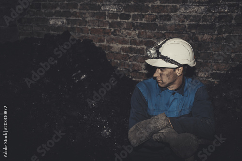 a miner with a pick sitting on the corner all tired and dirty from the coal dust after a hard work in the mine