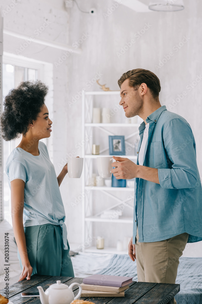 Obraz premium Young multiracial couple holding cups with coffee at home