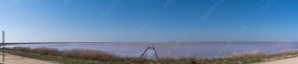 Pink salty lake with an old wooden pier. An ancient method of extracting salt from the sea.