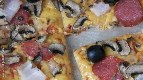 Big Italian pizza with black olives, bacon, salami and cheese close up. Hand takes a piece photo