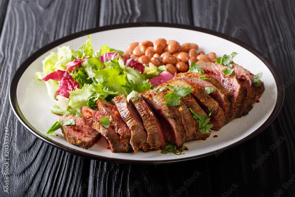 Serving grilled beef steak with fresh salad and beans close-up on a plate. horizontal Serving grilled beef steak with fresh salad and beans close-up on a plate. horizontal