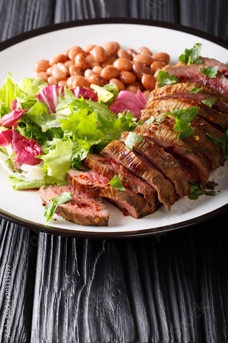 Grilled beef steak with green salad and beans close-up on a plate. vertical