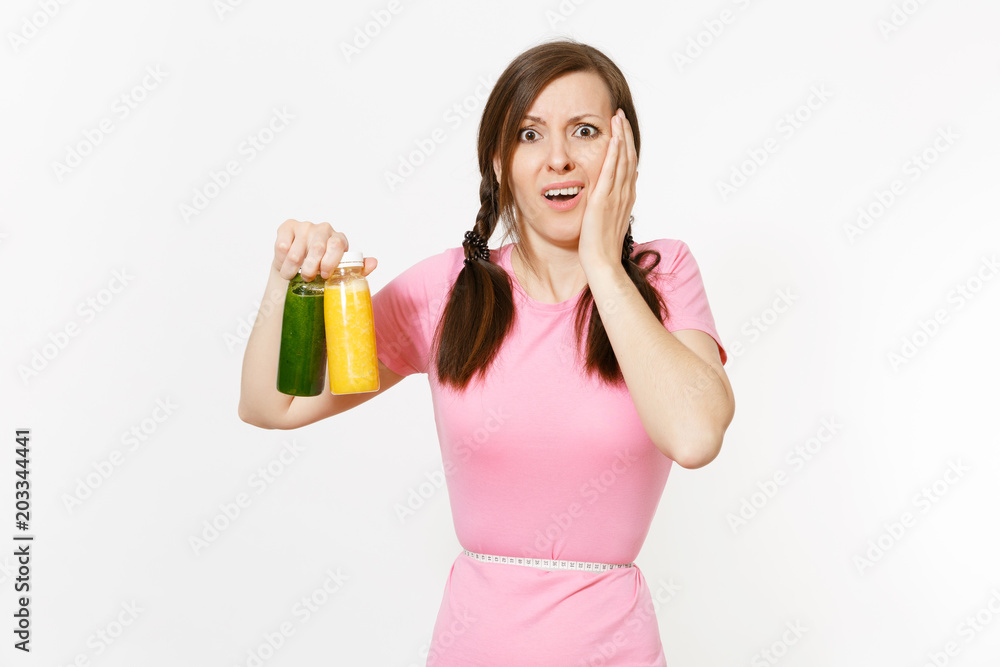 Sad woman holds green, yellow detox smoothies in bottles, measure tape on waist isolated on white background. Proper nutrition, vegetarian drink, healthy lifestyle, dieting concept. Copy space, flack. Sad woman holds green, yellow detox smoothies in bottles, measure tape on waist isolated on white background. Proper nutrition, vegetarian drink, healthy lifestyle, dieting concept. Copy space, flack.