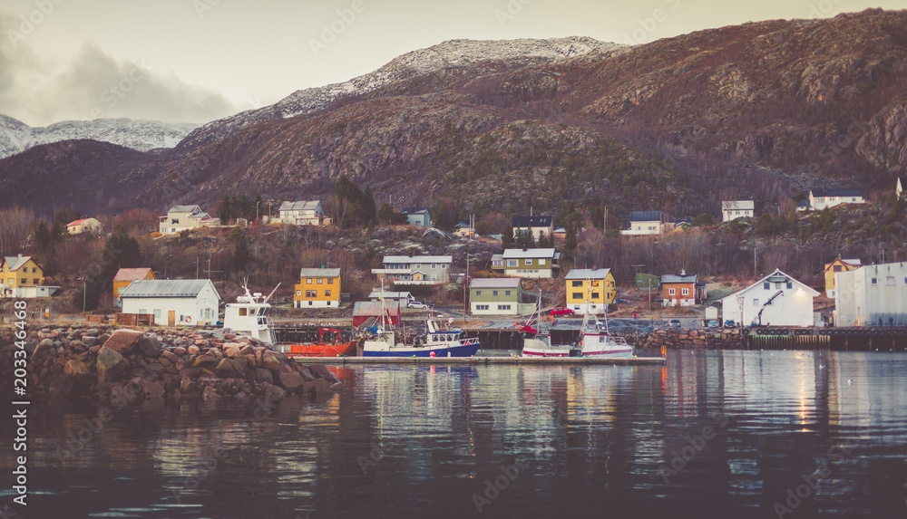 Harbor in a little fisherman village with moored boats and yachts with snow-capped peaks in the background.