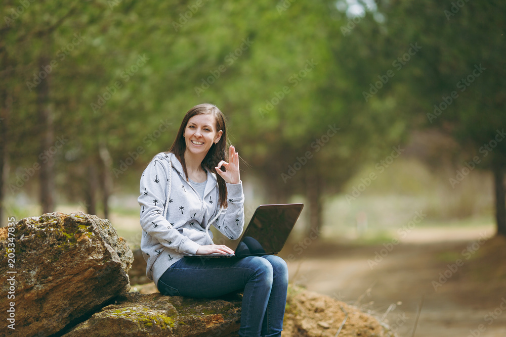 Young successful smart business woman or student in casual clothes sitting  on stone using laptop and