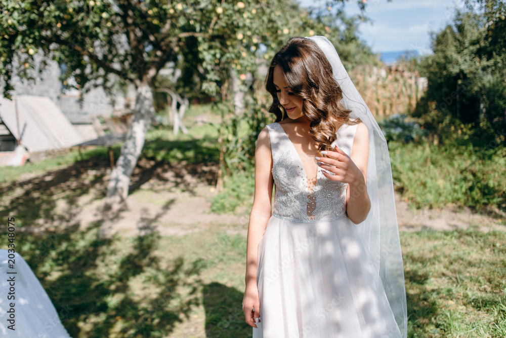 Naklejka premium Bride's morning in the garden. Fine art wedding. Portrait of a young beautiful sexy tender bride with red lips in white lace dress. Closeup view