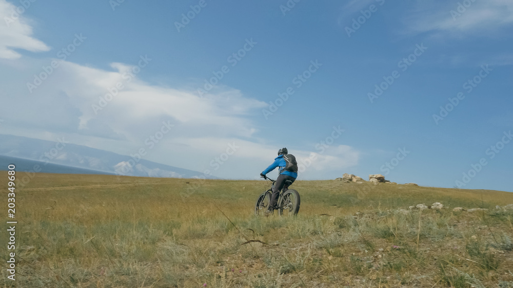 Fat bike also called fatbike or fat-tire bike in summer driving through the hills. The guy is riding a bike along the sand and grass high in the mountains. He performs some tricks and runs dangerously Fat bike also called fatbike or fat-tire bike in summer driving through the hills. The guy is riding a bike along the sand and grass high in the mountains. He performs some tricks and runs dangerously