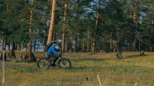 Fat bike also called fatbike or fat-tire bike in summer riding in the forest. The guy rides a bicycle among trees and stumps. He overcomes some obstacles on a bumpy road.