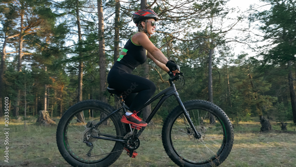 Naklejka premium Fat bike also called fatbike or fat-tire bike in summer riding in the forest. Beautiful girl and her bicycle in the forest. She rolls her bike and poses to the operator.