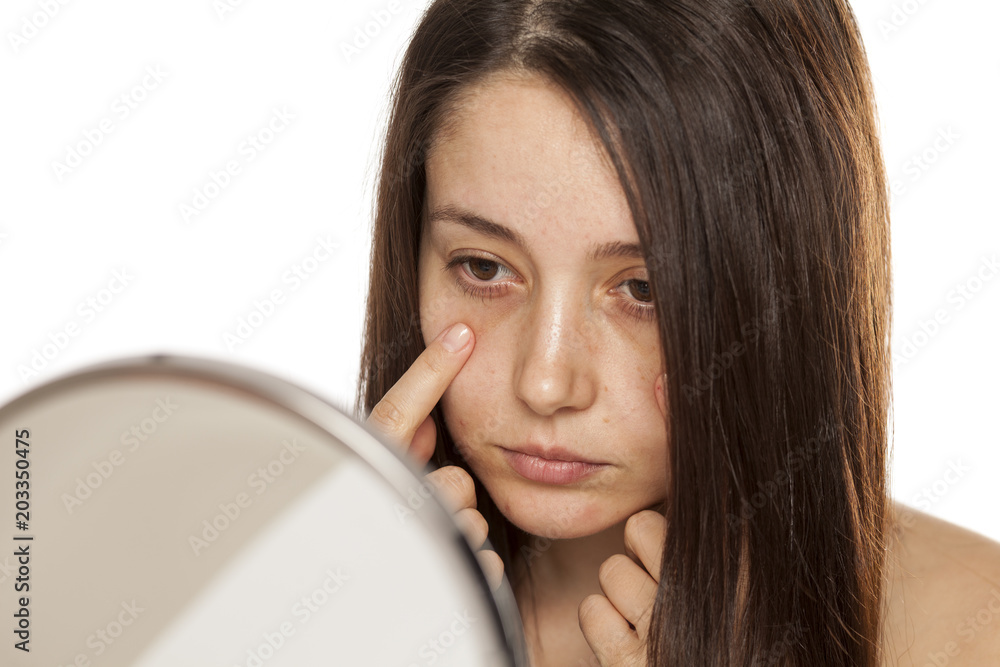 Unsatisfied young woman touch her face in mirror on white background Unsatisfied young woman touch her face in mirror on white background