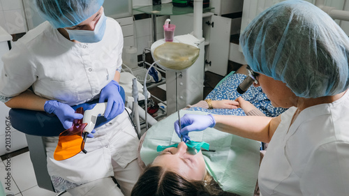 Tableau sur toile Woman at dentist clinic gets dental treatment to fill a cavity in a tooth