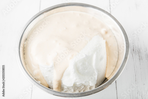 Cooking in the kitchen: egg yolks whipped with sugar mixed with whipped whites with one bowl on a white wooden background, top view