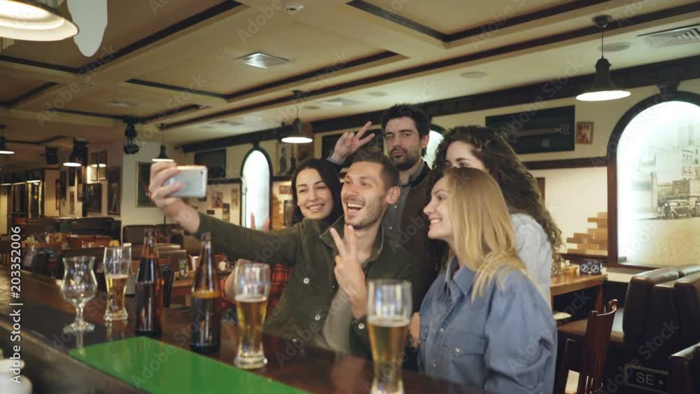Group of friends are taking selfie via smartphone in nice pub. Beautiful people in casual clothes are posing and having fun. Friendly relaxing atmosphere, happiness concept. Group of friends are taking selfie via smartphone in nice pub. Beautiful people in casual clothes are posing and having fun. Friendly relaxing atmosphere, happiness concept.