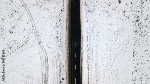 Top view from the air on the winter road in the field on which cars are going