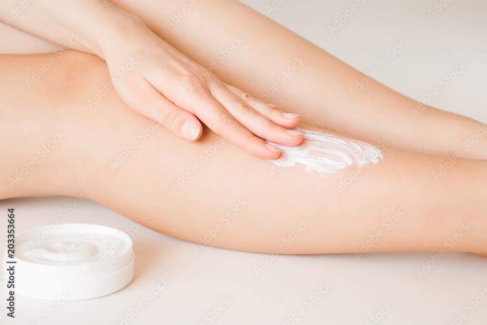 Fototapeta premium Beautiful, elegant woman's hands applying moisturizing cream on her leg. Jar with natural herbal cream. Cares about clean and soft legs skin. Healthcare concept.