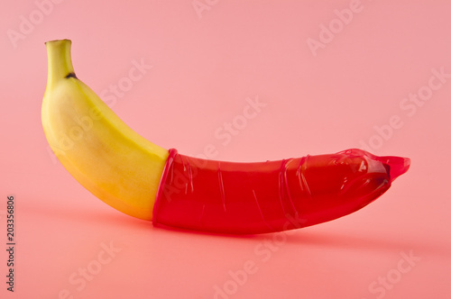 Banana with a red condom on a pink background. Safe sex concept