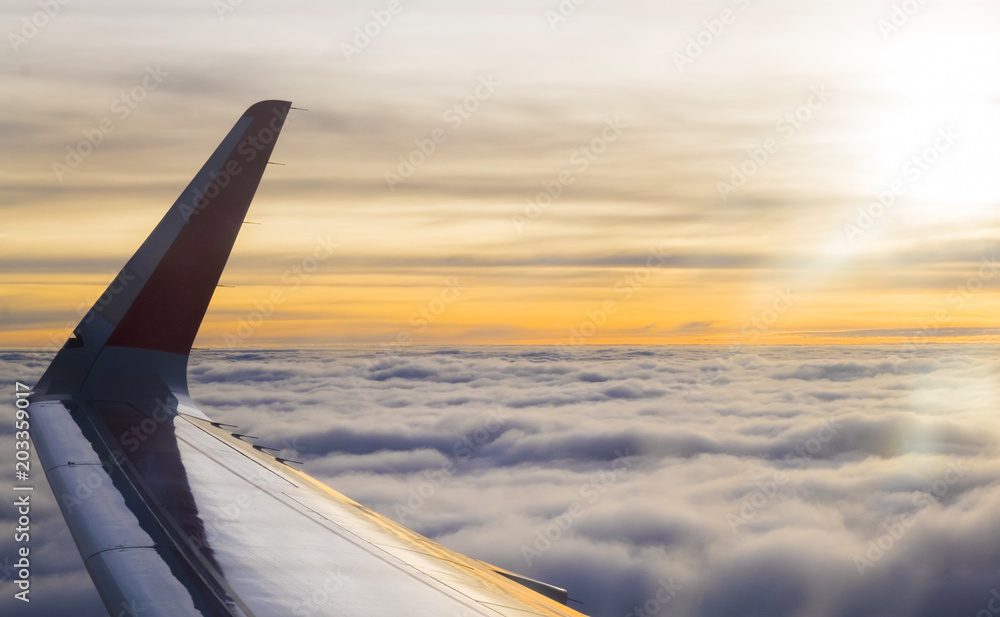 Wing of airplane flying above clouds at beautiful sunset