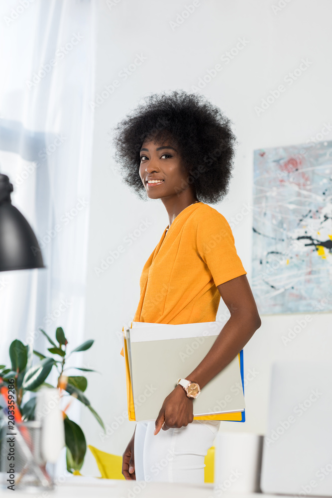 side view of smiling african american freelancer with papers in hand at home office