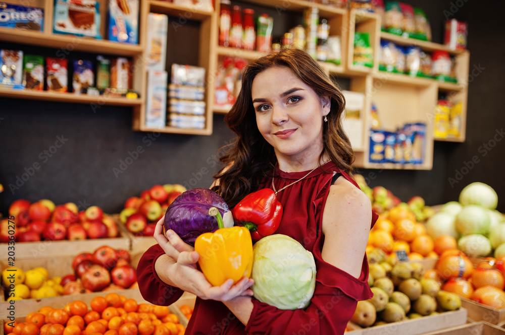 Girl in red holding different vegetables on fruits store. Girl in red holding different vegetables on fruits store.