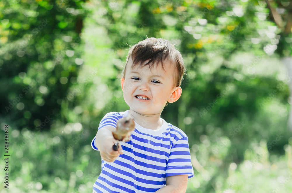 A child eats a kebab on a skewer, in a Park or forest nature green background of trees and grass A child eats a kebab on a skewer, in a Park or forest nature green background of trees and grass