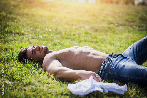Good looking, shirtless fit male model relaxing lying on the grass, shot from above