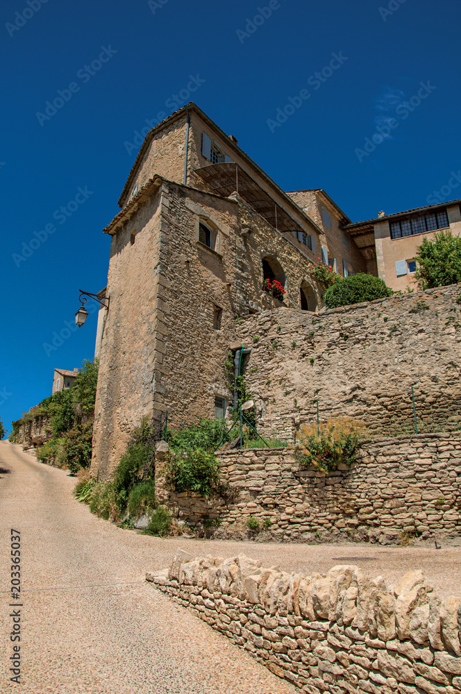 View of typical stone houses and wall with sunny blue sky, in alley of the historical city center of Gordes. Located in the Vaucluse department, Provence region, southeastern France