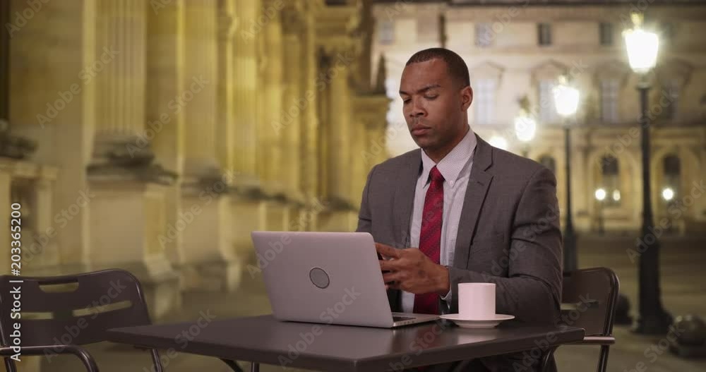 African-American businessman sitting at a public table using his laptop ...