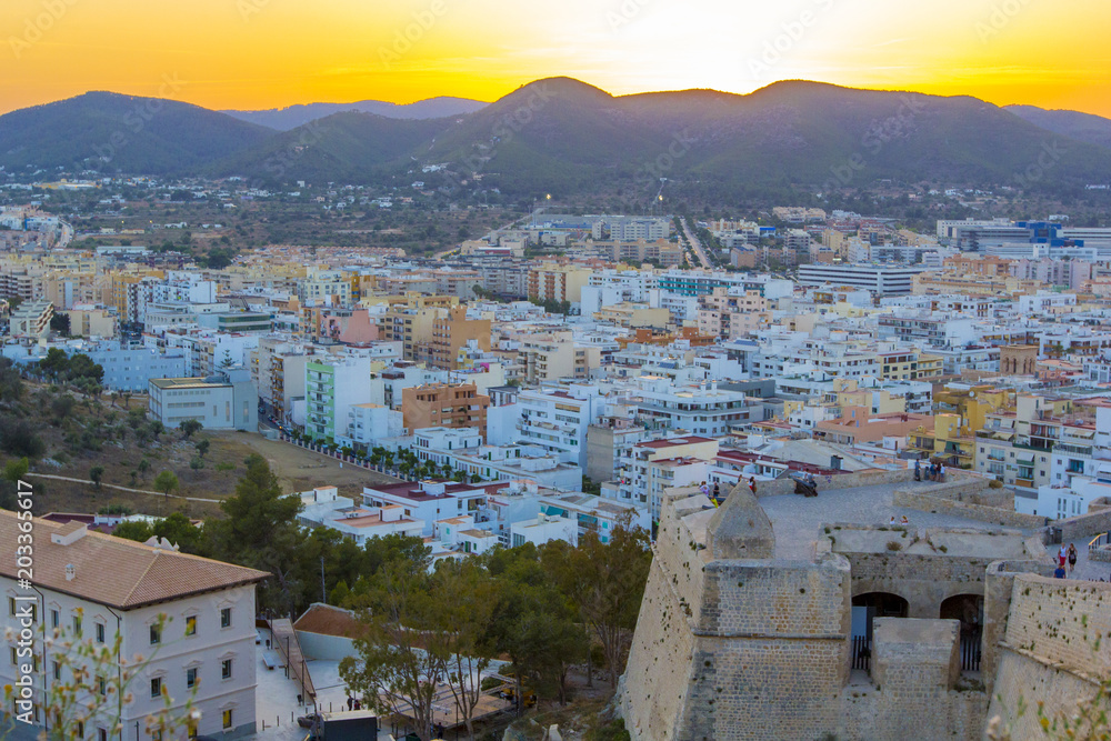 Panoramic view from medieval fortress on old town, streets and roofs of houses and mountains in evening light of street lamps and sunset, Ibiza, Balearic Islands, Spain