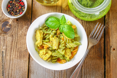 Pasta with chicken pieces and pesto sauce on an old wooden table.