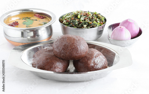 Ragi or finger millet balls, which are a healthy south Indian food, in a tray with sambar, horse gram-amaranth leaves curry and raw onions.