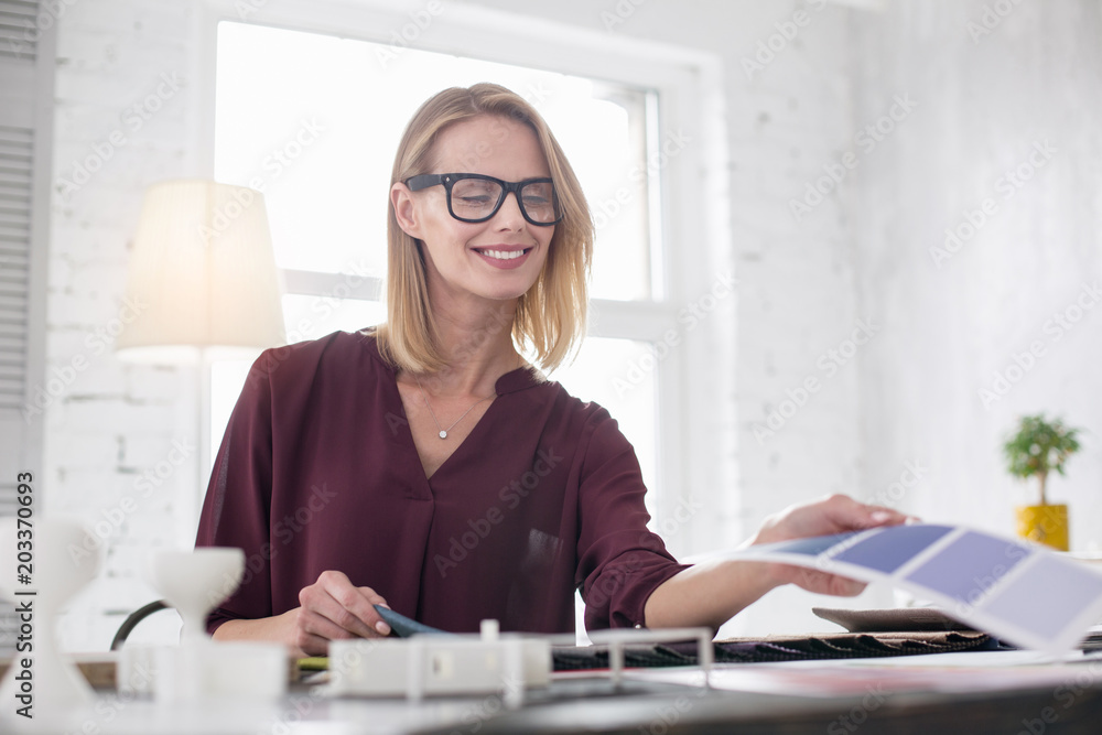 Pleasure in work. Vigorous female designer putting on glasses and choosing upholstery