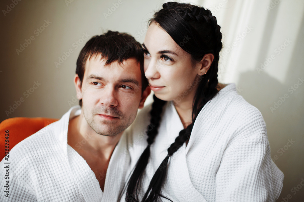 Young husband and wife of white coats play and smile in an orange armchair in a hotel room. Close up.