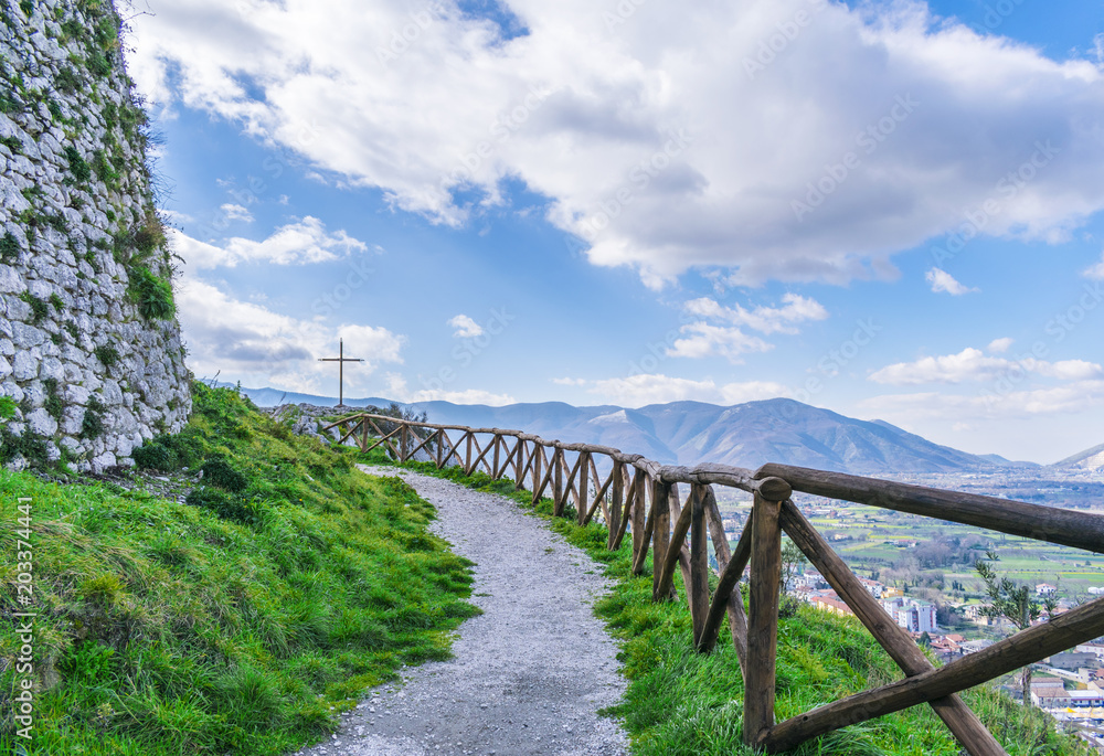 Beautiful landscape, mountain path with a wooden fence and steel cross. The Italian Apennines.