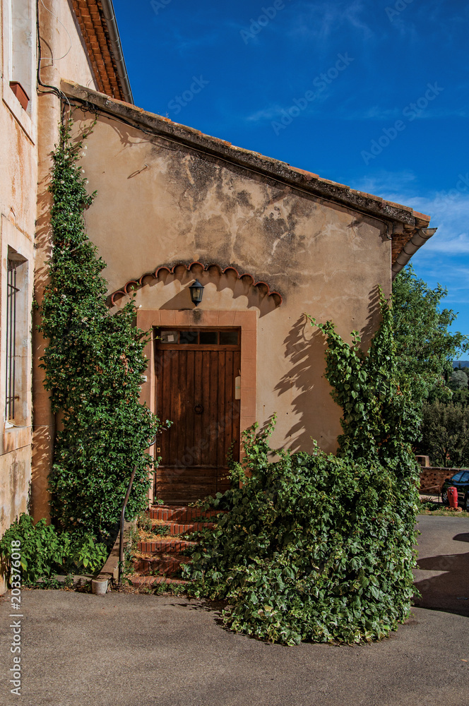 View of traditional colorful house in ocher and bindweed under a sunny blue sky, in the city center of Roussillon village. Located in the Vaucluse department, Provence region, southeastern France