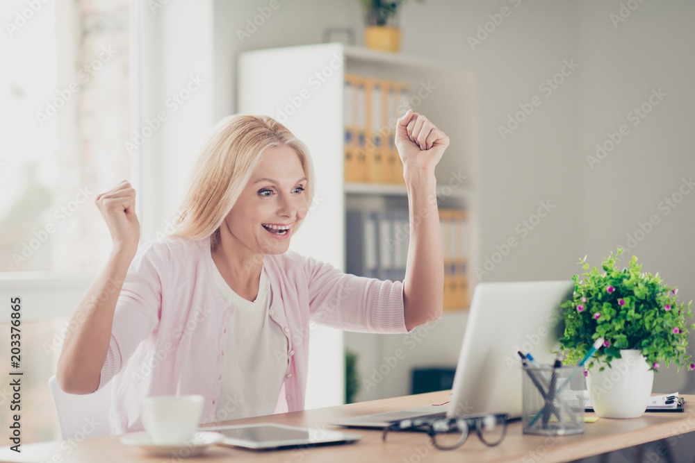 Attractive, stylish, modern, pretty, charming, aged woman looking at screen of computer raised hands celebrating successfully completed work, project, presentation, sitting at desktop in work station Attractive, stylish, modern, pretty, charming, aged woman looking at screen of computer raised hands celebrating successfully completed work, project, presentation, sitting at desktop in work station