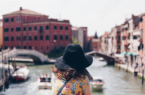 Fototapeta Naklejka Na Ścianę i Meble -  Back view of a Girl with hat standing on the bridge over the canal at the Venice - Italy