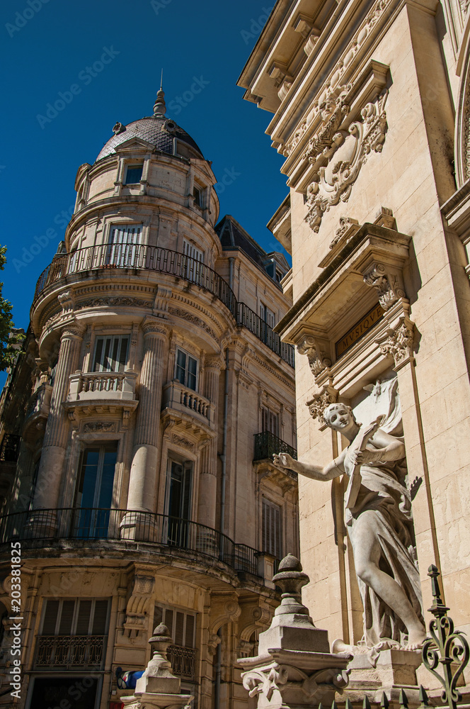 Close-up of buildings in the city center of Nimes, with statues, decorative details on the walls and blue sky. Located in the Gard department, Occitanie region in southern France