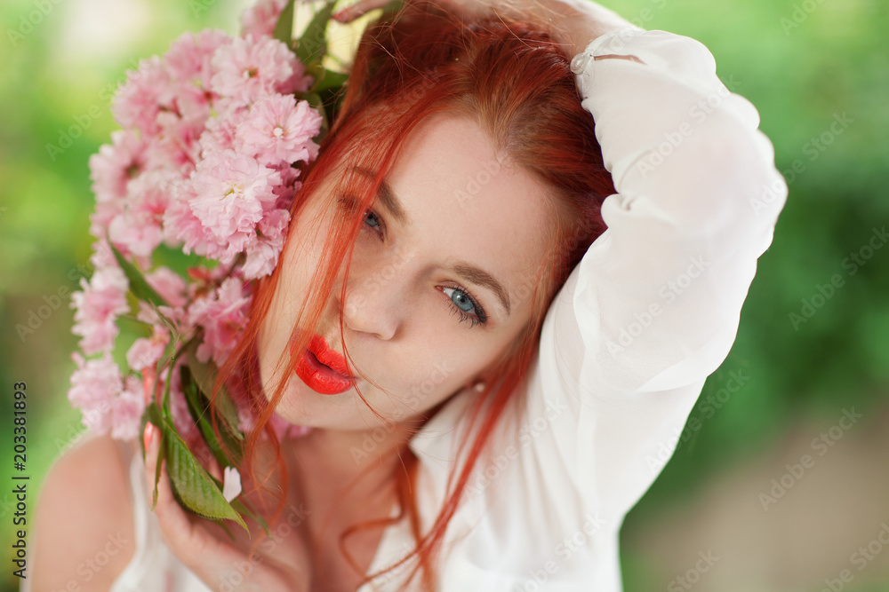 Beautiful young woman with red hair having fun standing in the garden with cherry blossom branch and perfect make up Beautiful young woman with red hair having fun standing in the garden with cherry blossom branch and perfect make up